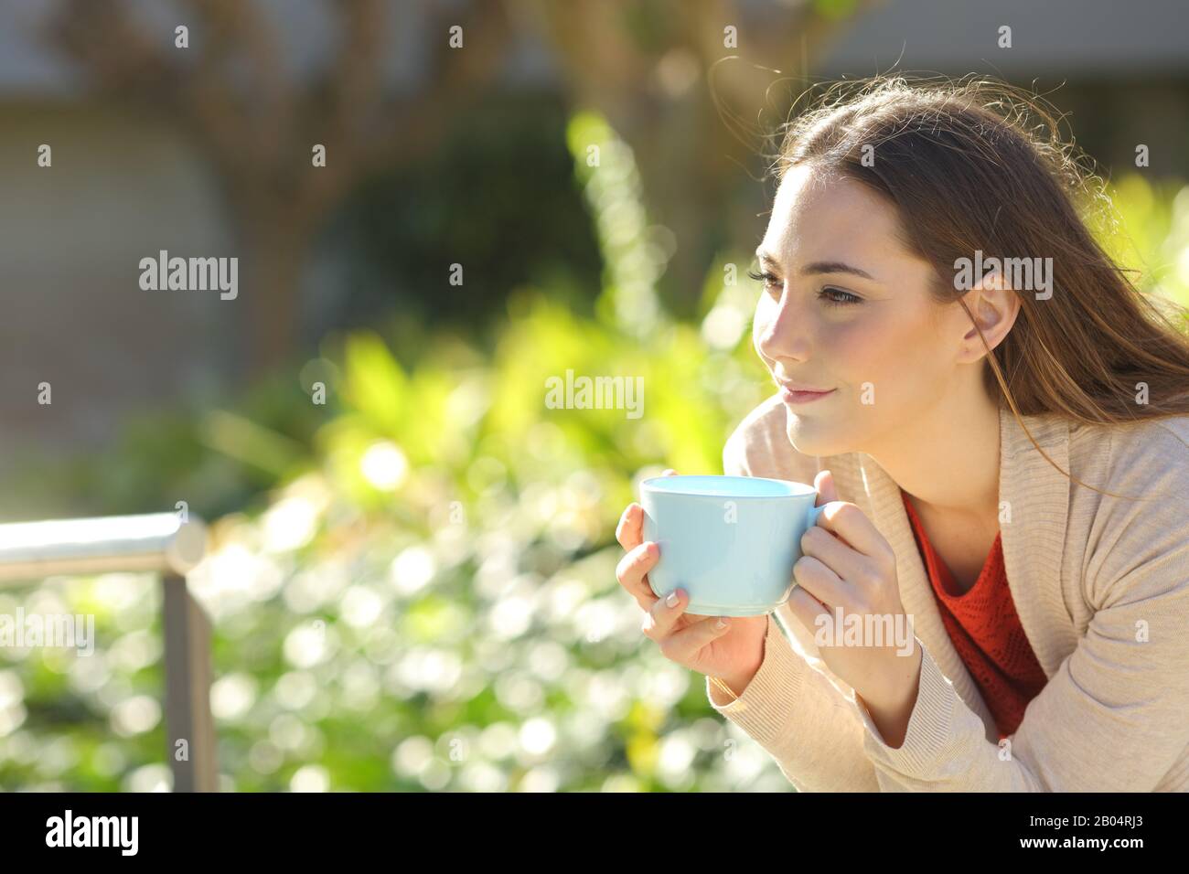 Eine entspannte Frau, die eine Tasse Kaffee hält und im Park sitzt Stockfoto