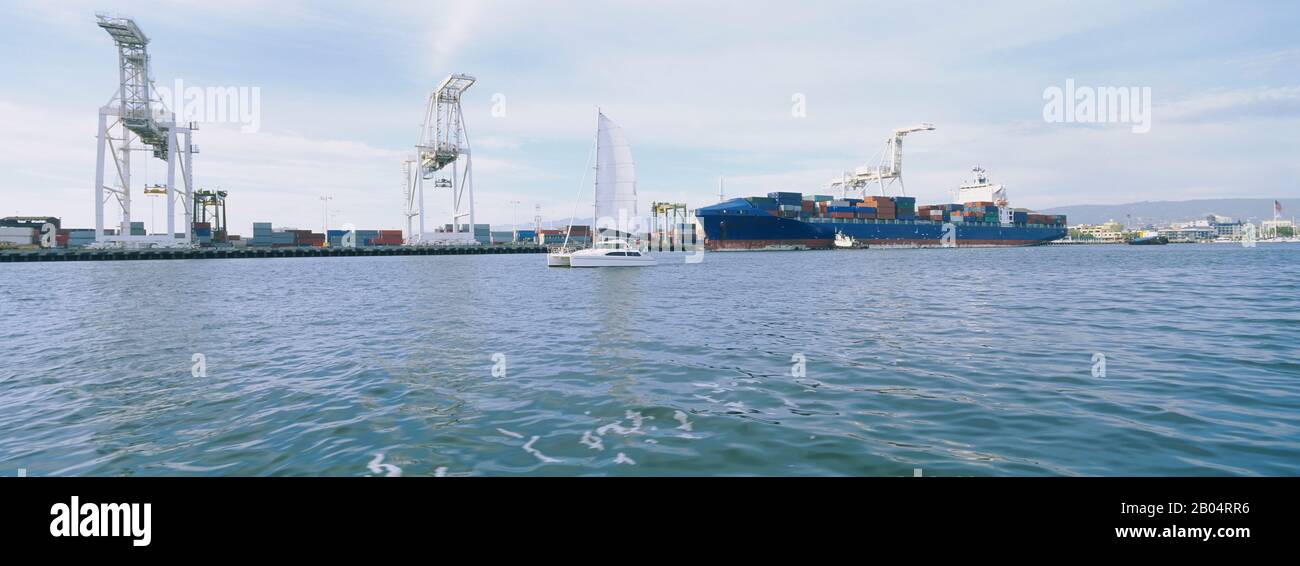 Segelboot und Containerschiff vor einem Handelsdock, Port Of Oakland, San Francisco, Kalifornien, USA Stockfoto