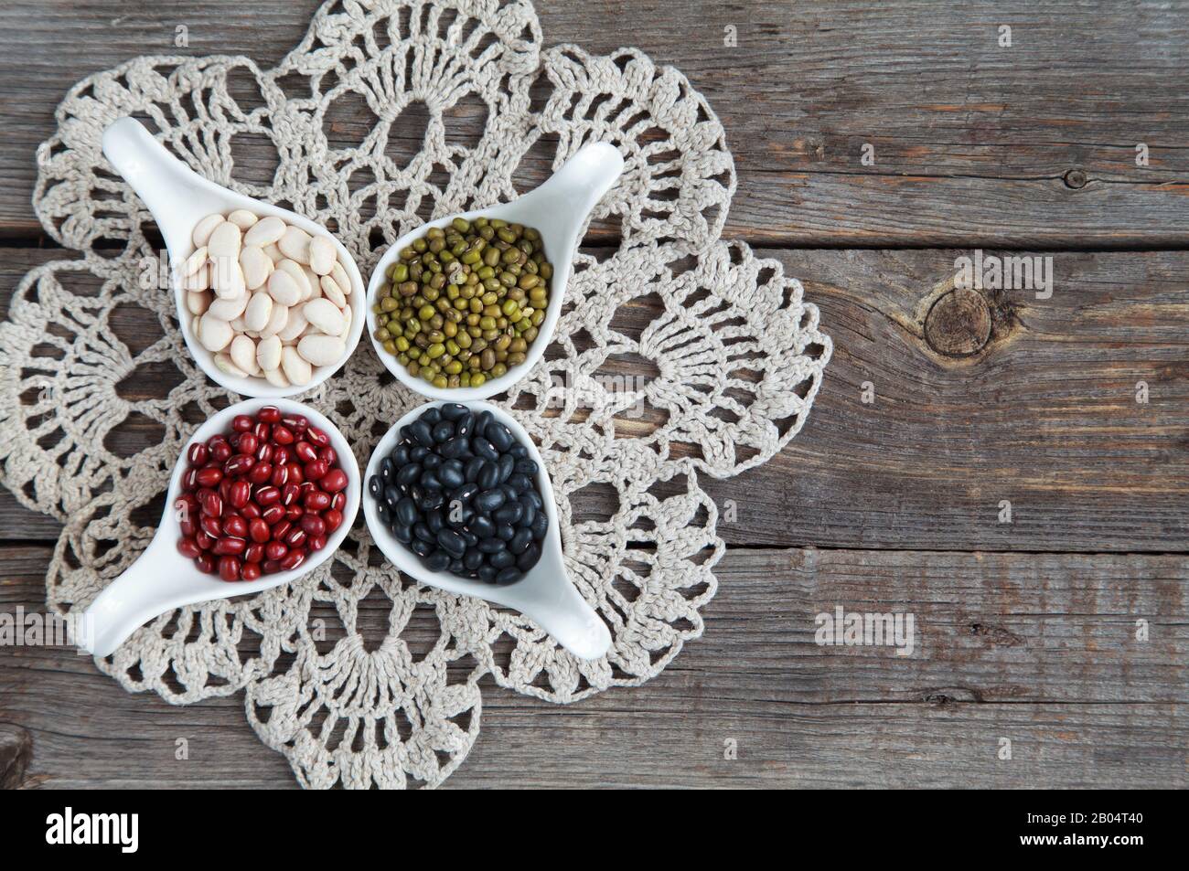 Verschiedene Sorten Bohnen: Baby lima, schwarz klein, Adzuki und Mang in weißen Keramiklöffeln (Vorspeisen) auf Holzgrund, selektives lwl Stockfoto