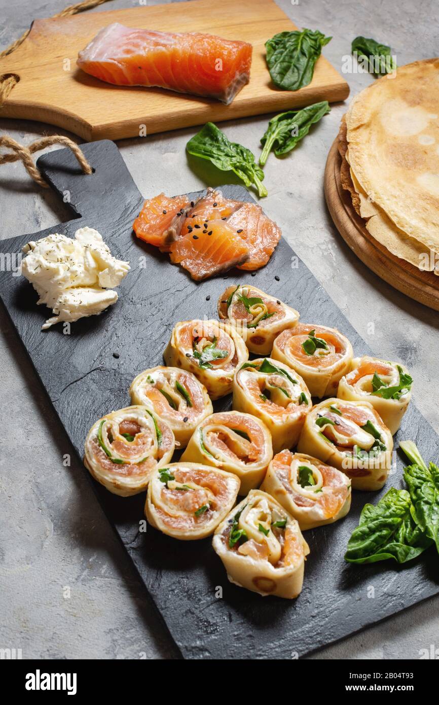 Pfannkuchenrollen mit Räucherlachs und Frischkäse auf Betongrund. Stockfoto