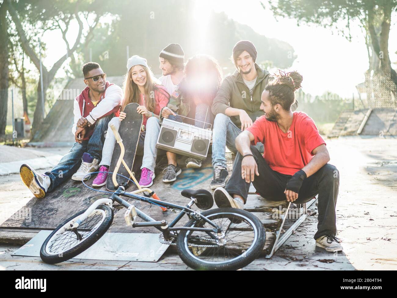 Junge Freunde, die Musik hören und im Stadtpark lachen - Gruppe von mehrjährigen Menschen, die gemeinsam Spaß haben - Jugend, urbaner Lebensstil, Multira Stockfoto