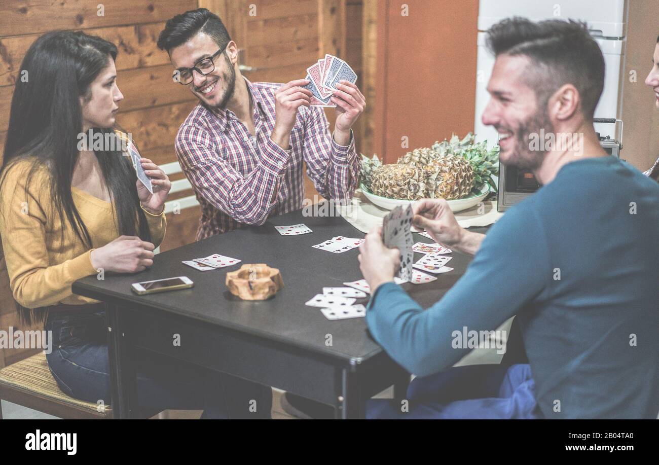 Eine Gruppe von Freunden, die Karten spielen, die an einem Tisch in den Ferien sitzen, Camping Haus - Junge glückliche Leute, die Spaß haben, zusammen zu lachen - Soft Focus Stockfoto