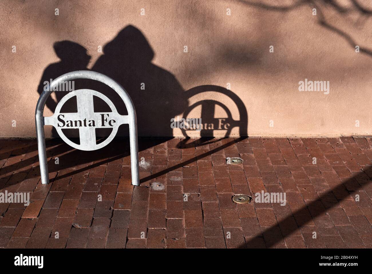 Touristen werfen einen Schatten, wenn sie an einem Fahrradträger auf einem Bürgersteig in Santa Fe, New Mexico, vorbeilaufen. Stockfoto