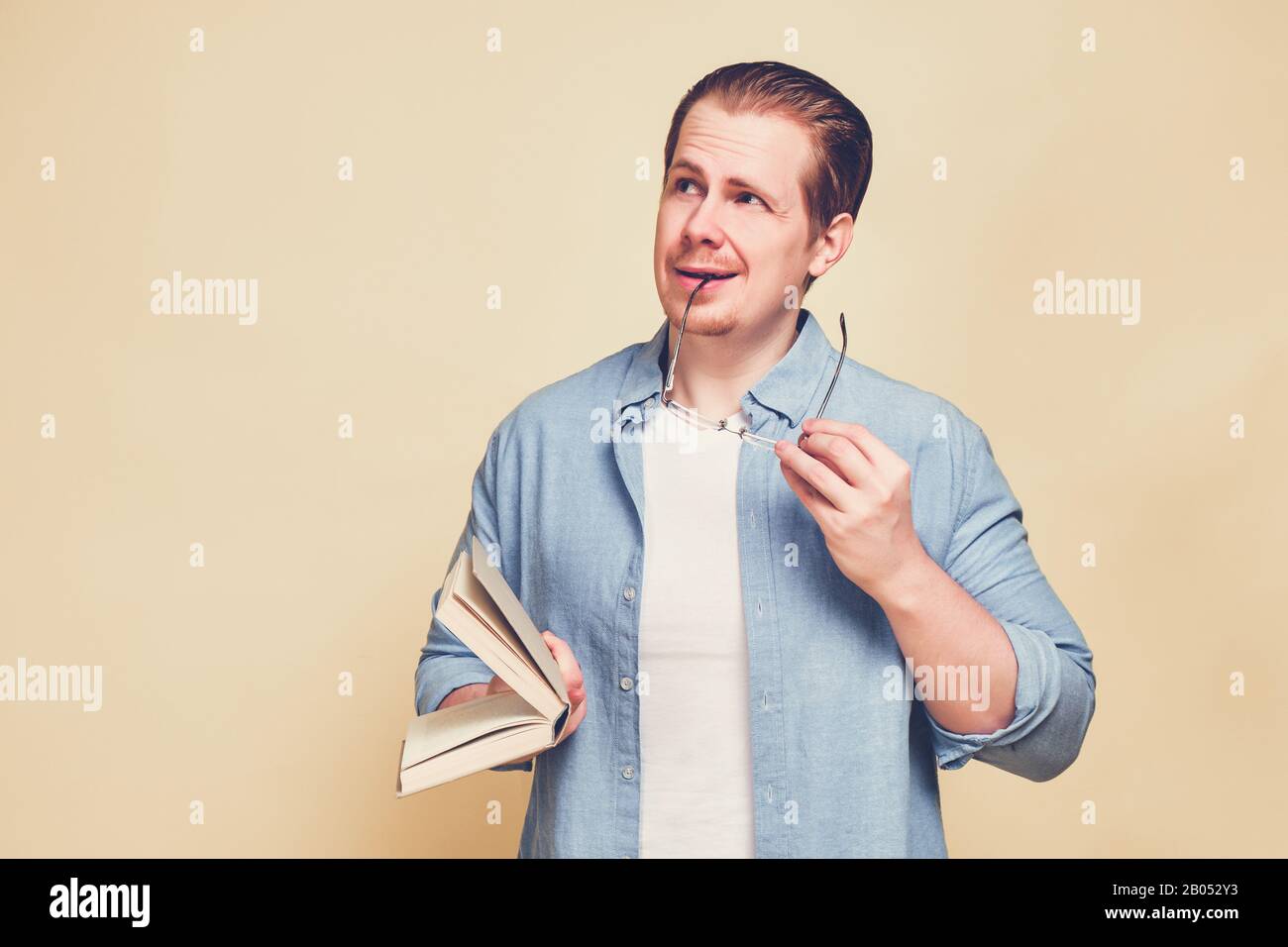 Ein Mann in einem blauen Hemd auf gelbem Hintergrund mit Brille und hält ein Buch mit einem nachdenklichen Look. Getont. Nahaufnahme. Stockfoto