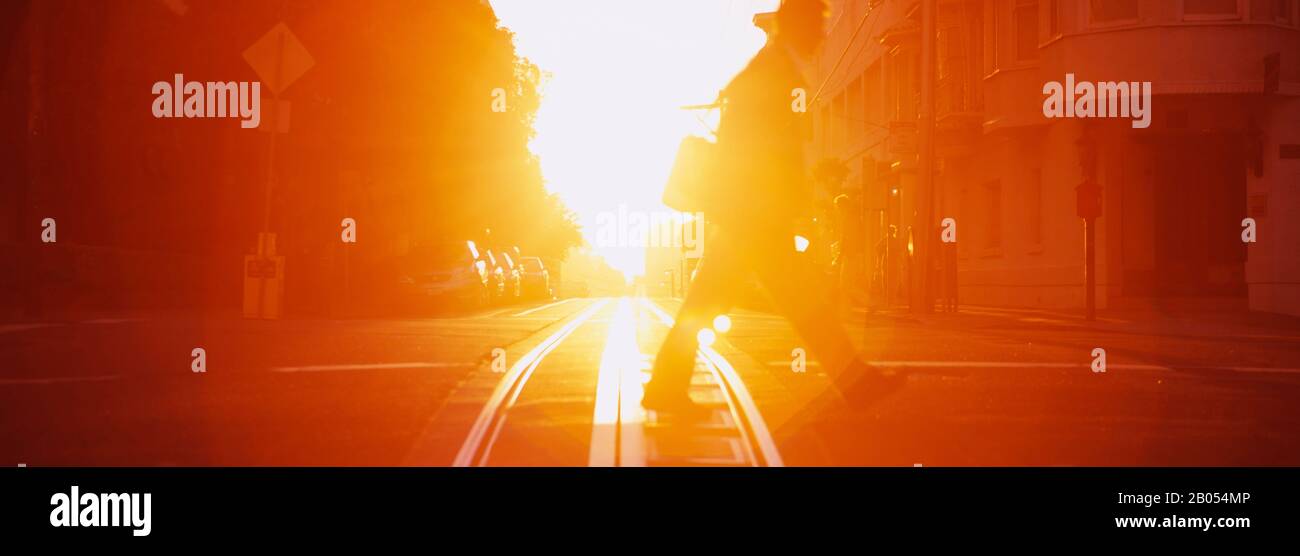 Seitenprofil einer Person, die die Seilbahngleise bei Sonnenuntergang überquert, San Francisco, Kalifornien, USA Stockfoto