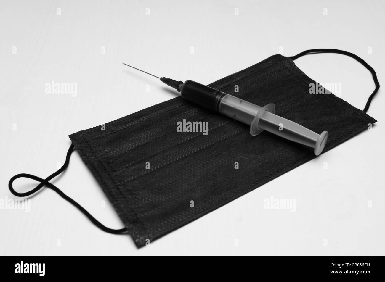 Schwarze medizinische Schutzmaske und Spritze mit schwarzem Inhalt auf weißem Hintergrund. Das Konzept der tödlichen Krankheit. Schwarz-Weiß-Bild Stockfoto