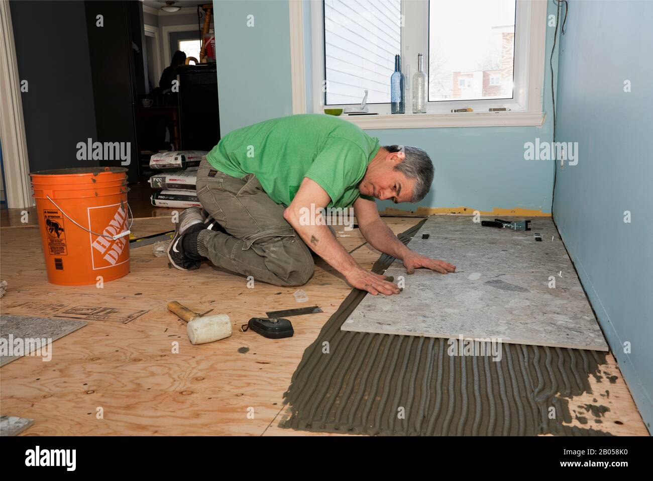 Arbeiter, der graue keramische Bodenfliesen über eine Schicht Klebzement legt. Stockfoto