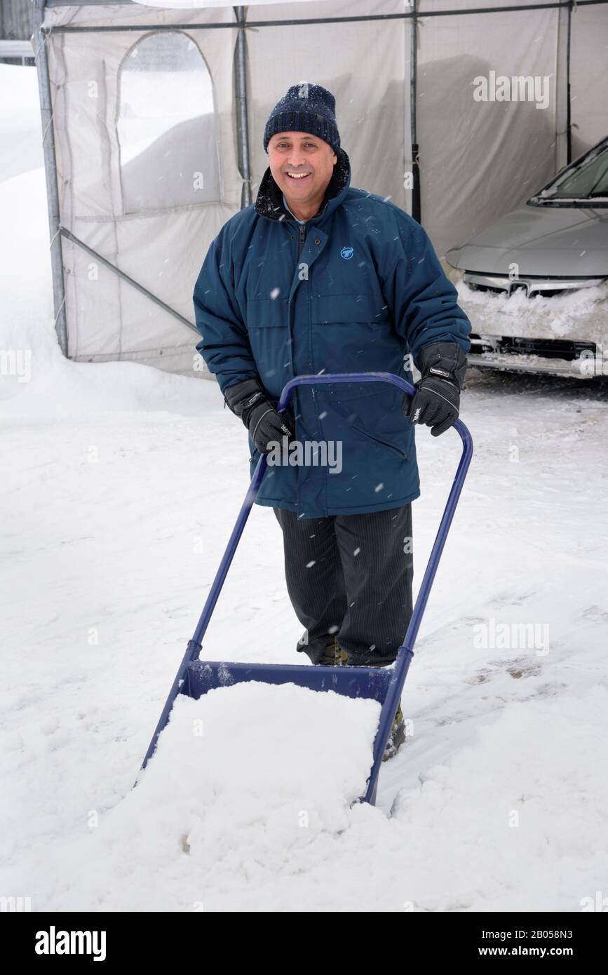 Mann entfernt mit einer Schlittenschaufel Schnee von seiner Einfahrt. Provinz Quebec, Kanada. Stockfoto