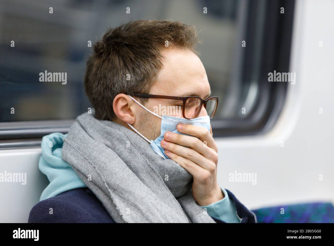 Nahaufnahme des kranken Mannes in Brillen, die in Schal gewickelt waren, sich krank fühlend, hustend, Schutzmaske gegen übertragbare Infektionskrankheiten tragend, Kovid-19 Stockfoto