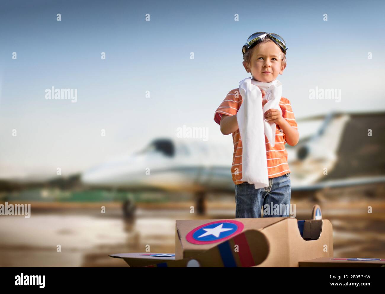 Der junge Junge in seinem Pappkartonflugzeug träumt davon, eines Tages ein echtes Flugzeug zu fliegen. Stockfoto
