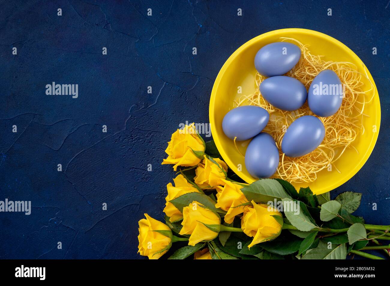 Osterzusammensetzung mit gelben Rosen und Eiern auf dunkelblauem Grund Stockfoto