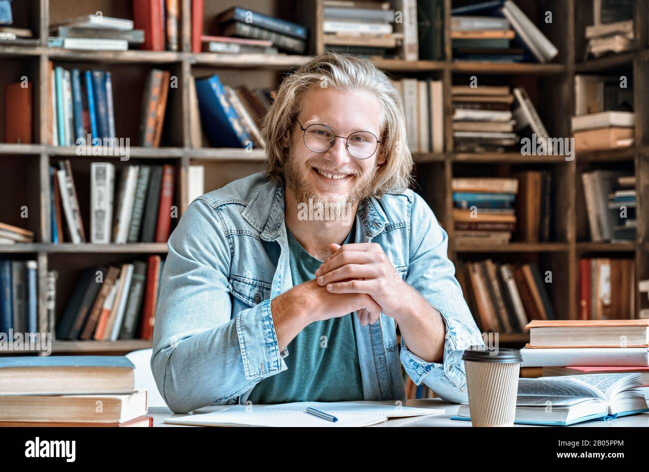 Portrait junger Student am Schreibtisch der Bibliothek lächelt auf die Kamera Stockfoto
