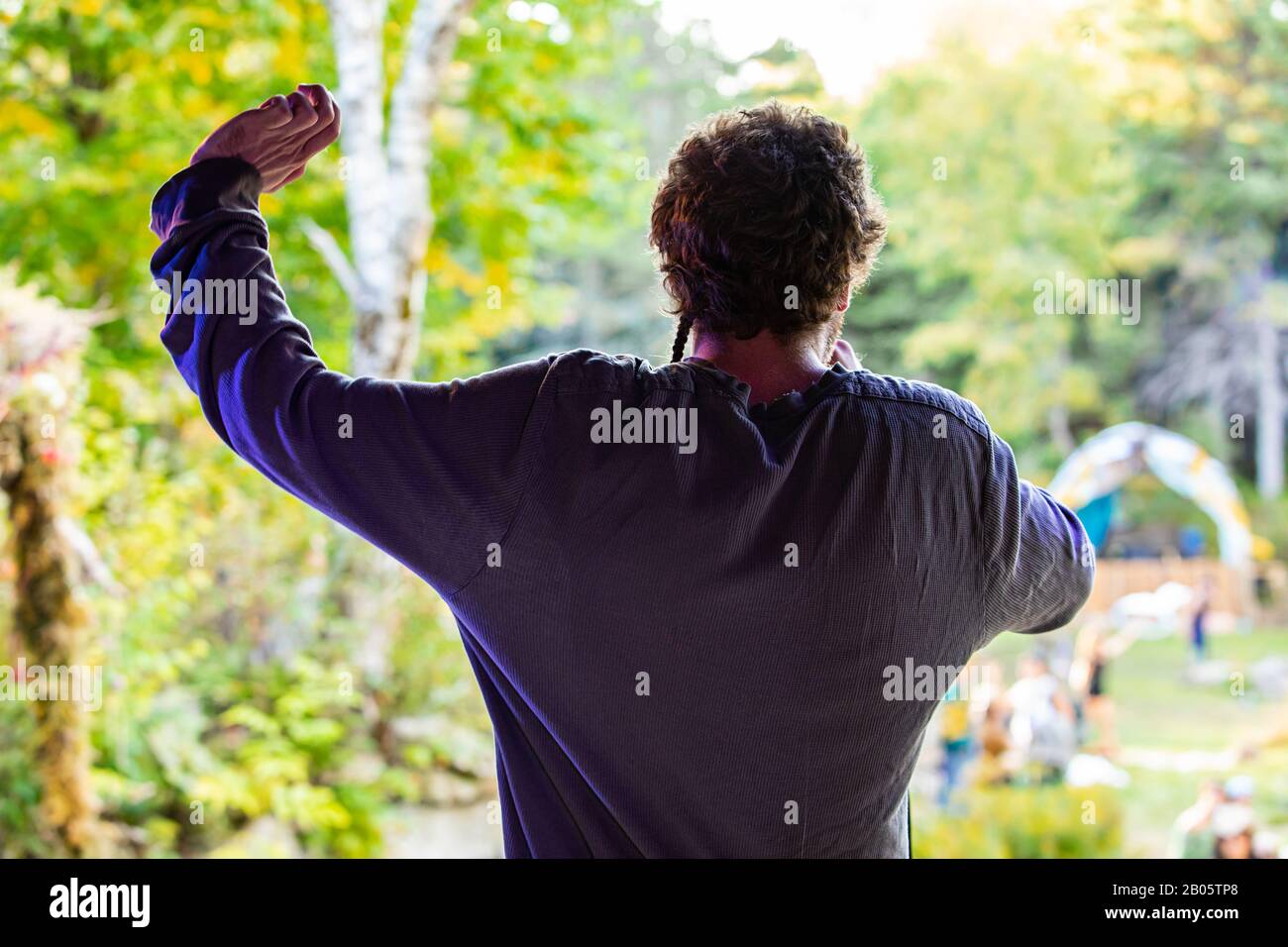 Ein Mannlicher Sanger Der Ein Sackiges Hemd Mit Kurzen Lockigen Haaren Tragt Wird Von Hinten Gesehen Und Steht Wahrend Eines Multikulturellen Festivals Mit Einem Erhobenen Arm Auf Der Buhne Stockfotografie Alamy