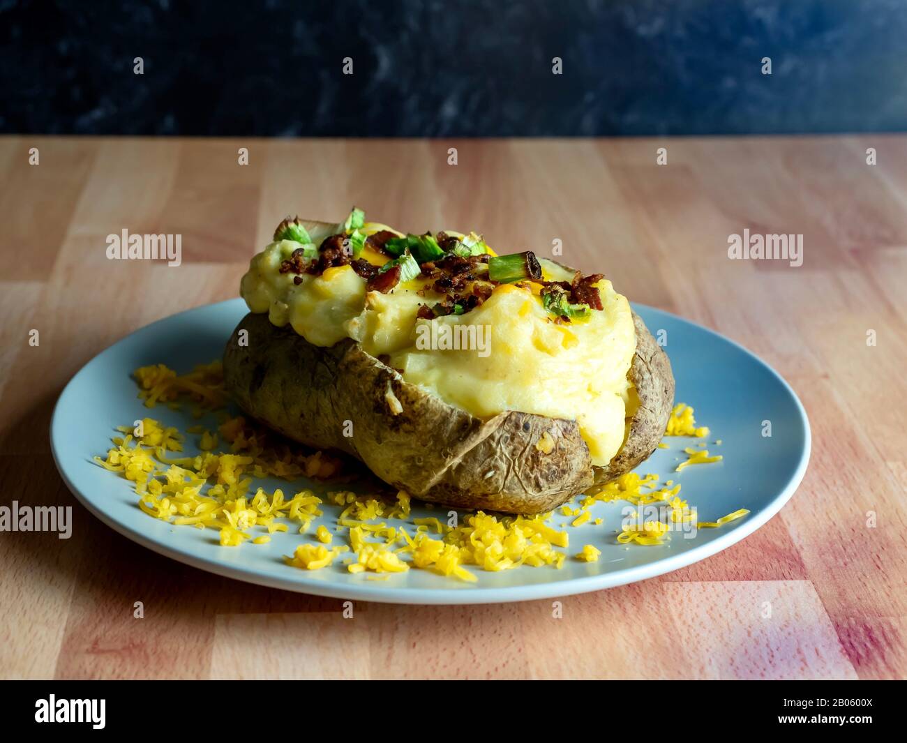 Hausgemachte, zweimal gebackene Kartoffel mit Cheddar-Käse, Speck und grünen Zwiebel-Hengsten auf einer grauen Platte vor einem Metzgerblock-Hintergrund. Stockfoto