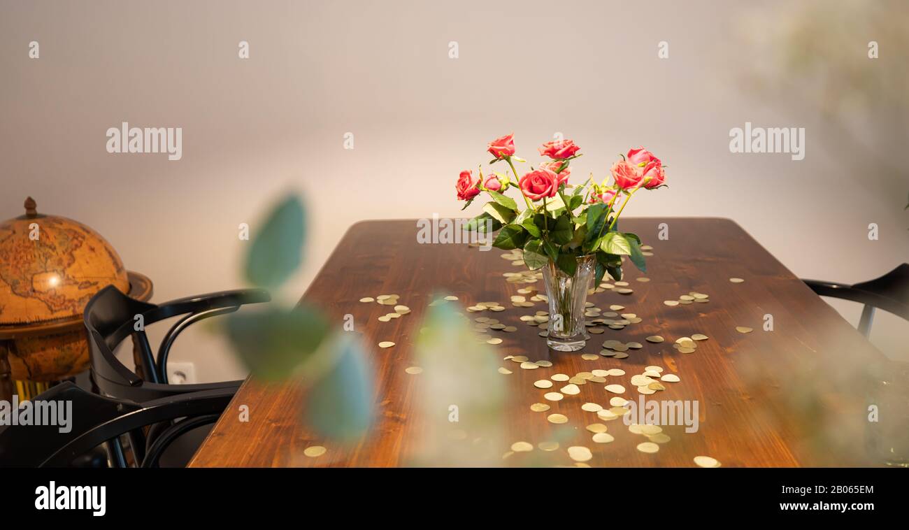 Vase mit roten Rosen auf einem Tisch mit goldenem Konfetti und einem Globus in der Ecke. Stockfoto