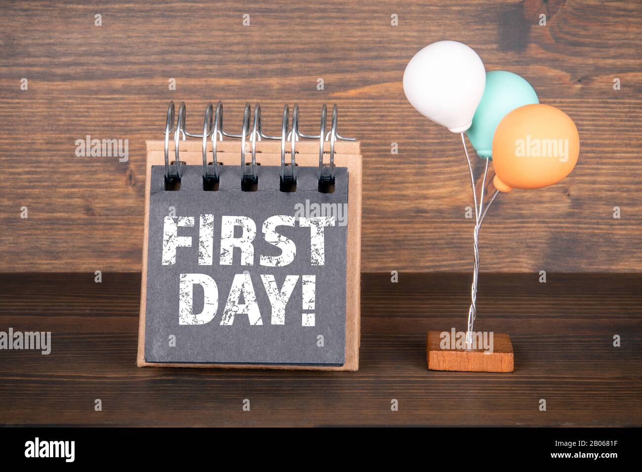 Erster Tag. Geburtstag, Arbeit, Schule und Urlaubskonzept. Notizbuch und bunte Ballons auf dem Holzhintergrund Stockfoto