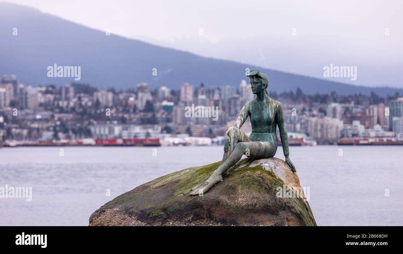 Vancouver, BC Canada - 14. März 2019: Eine Statue eines Mädchens in einem Badeanzug auf einem Felsbrocken an einem Ufer des Vancouver Harbour mit Blick auf die Stadt im Hintergrund Stockfoto