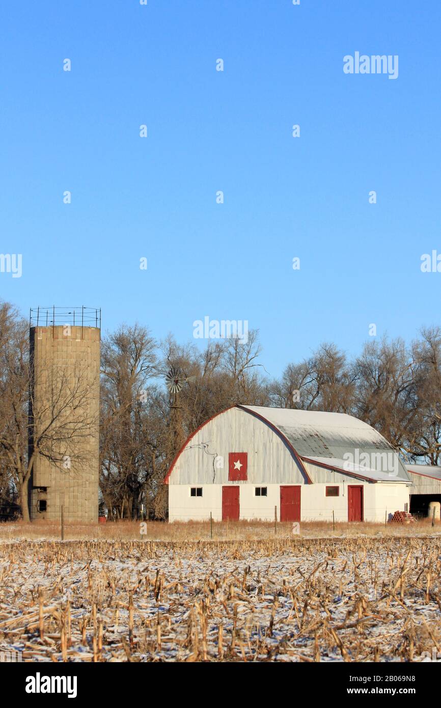 Kansas Country Barn mit Schnee, blauem Himmel und Corn-Stoppelung im Land mit Bäumen. Stockfoto