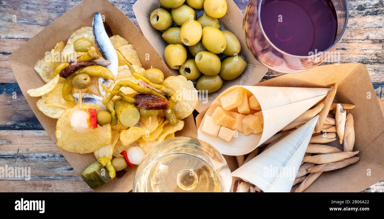 Tapas und Pinchos, Panorama-Blick über die Decke. Käse, Jamon und Oliven, gildas und Kartoffelchips, mit Brille aus Rot- und Weißwein, auf einem Holztisch Stockfoto