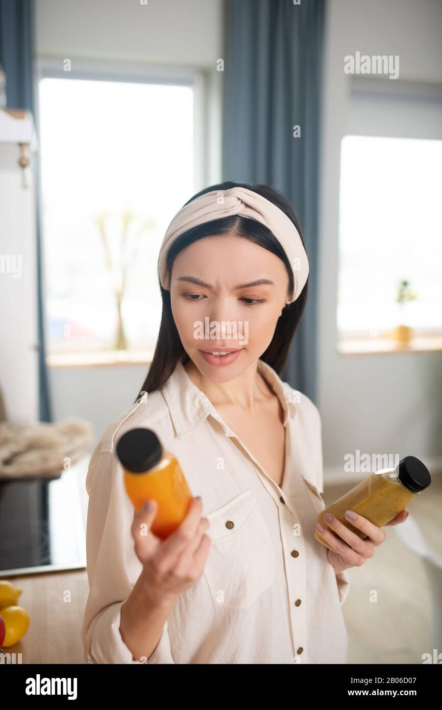 Ernsthafte junge Frau, die eine Flasche Saft in der Hand betrachtet. Stockfoto