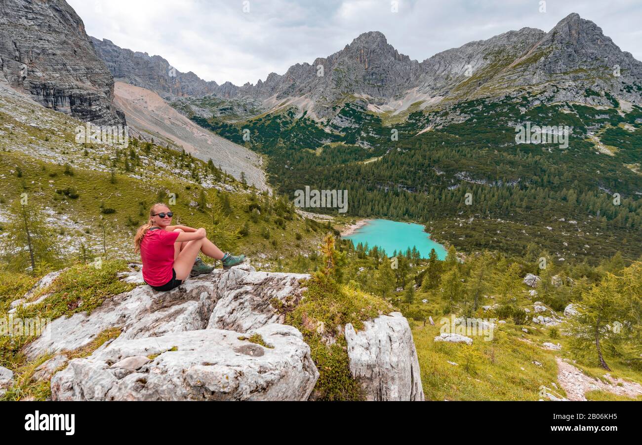 Junge Frau, Wanderer auf Felsen sitzend und mit Blick auf den türkisgrünen Sorapisser See und die Berglandschaft, die Dolmen, Belluno, Italien Stockfoto