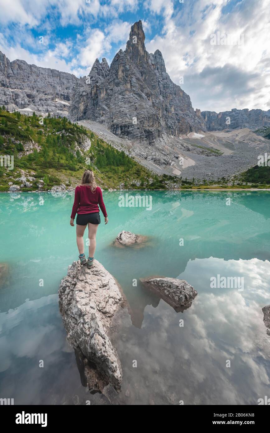 Junge Frau, Wanderer auf Felsen im Wasser am türkisgrünen Sorapis-See, Lago di Sorapis, Berggipfel Dito di Dio, in den Bergen, in den Bergen, Belluno Stockfoto