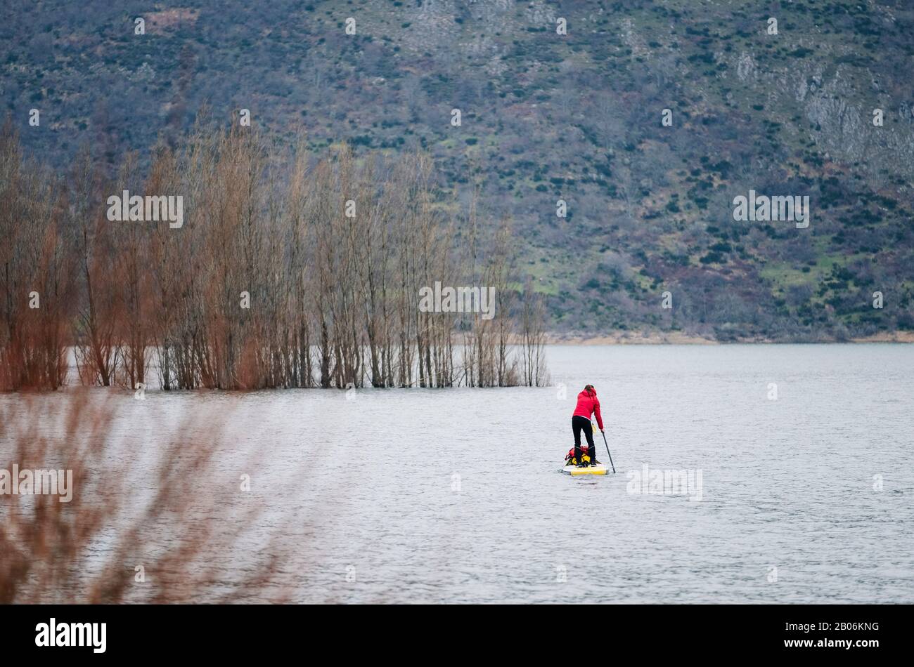 Ein Mädchen in einem roten Mantel surft auf einem Bergsee mit Gepäck auf ihrem Brett Stockfoto