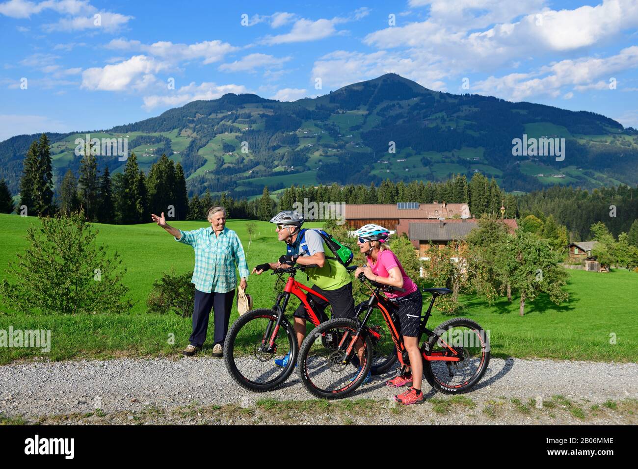 Die alte Bauernfrau zeigt zwei Radfahrer mit Elektro-Mountainbikes den Weg zum Glantersberg, im Hintergrund die hohe Salve, Kitzbüheler Alpen Stockfoto