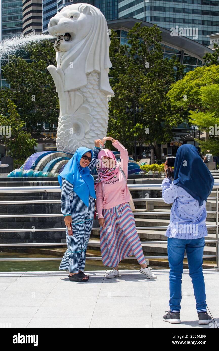 Zwei indonesische malaiische muslimische Damen mehrerer Generationen lächeln für die Kamera, die vor dem legendären Merlion, dem Merlion Park, posiert. Singapur. Stockfoto