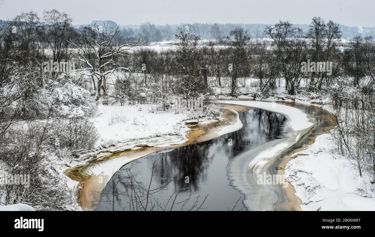 Blick auf den nicht gefrorenen Fluss. Winterlandschaft. Schnee auf dem Boden und Bäume im Wald. Bewölkter Tag. Stockfoto