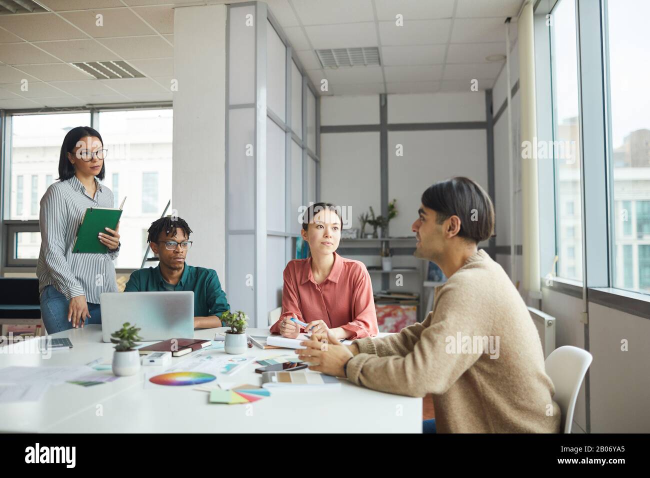 Der junge Geschäftsmann erzählt seinen Kollegen etwas, während sie im Team im Büro am Tisch arbeiten Stockfoto