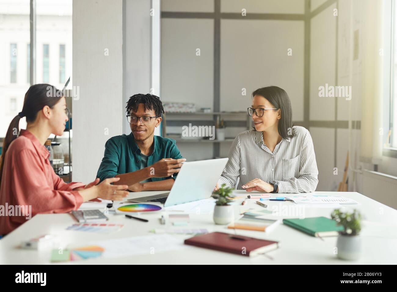 Junge Designer diskutieren die Präsentation im Team, während sie am Tisch mit Laptop und Muster im Büro arbeiten Stockfoto