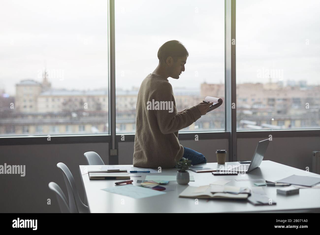 Junger Geschäftsmann, der auf dem Tisch sitzt und den Bericht vor dem Treffen im Büro prüft Stockfoto