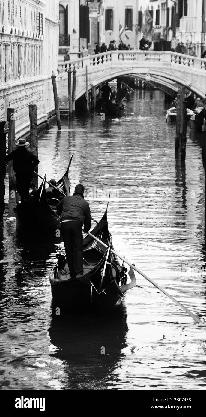 Stadt Venedig, Italien, Europa. Schwarz-Weiß-Bild von Gondoliers, die entlang des schmalen Kanals in Richtung Steinbrücke rudern Stockfoto