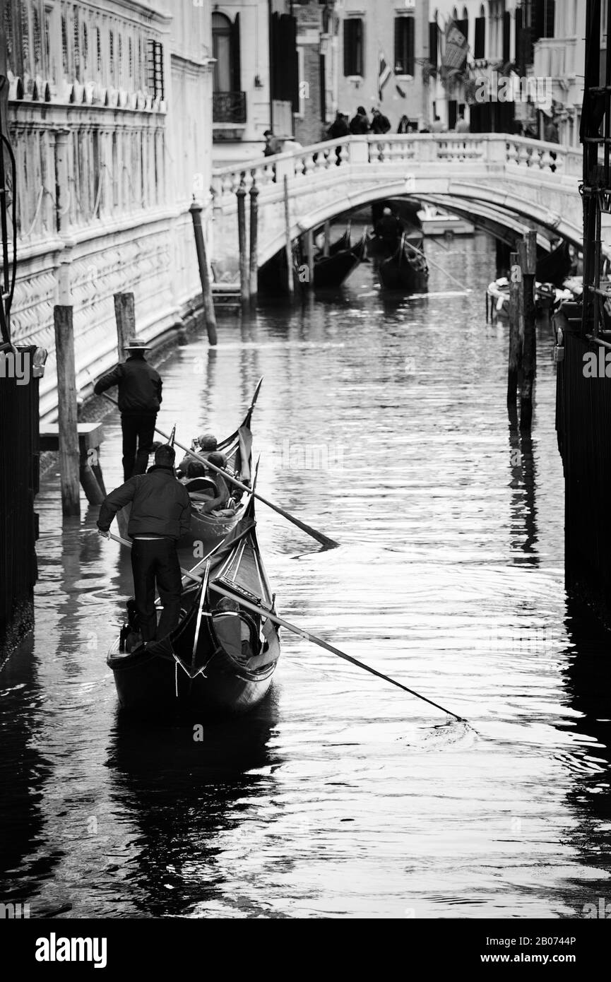 Stadt Venedig, Italien, Europa. Schwarz-Weiß-Bild von Gondoliers, die entlang des schmalen Kanals in Richtung Steinbrücke rudern Stockfoto