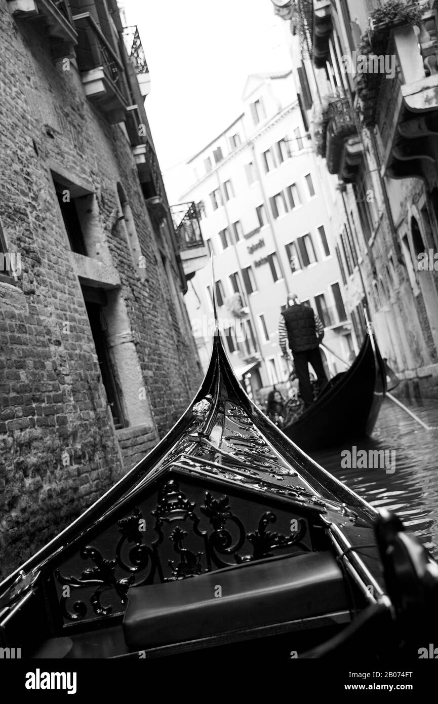 Stadt Venedig, Italien, Europa. Schwarz-Weiß-Bild auf der Gondel mit verzierter Vorderseite der Gondel. Enger Kanal mit hohen Gebäuden Stockfoto