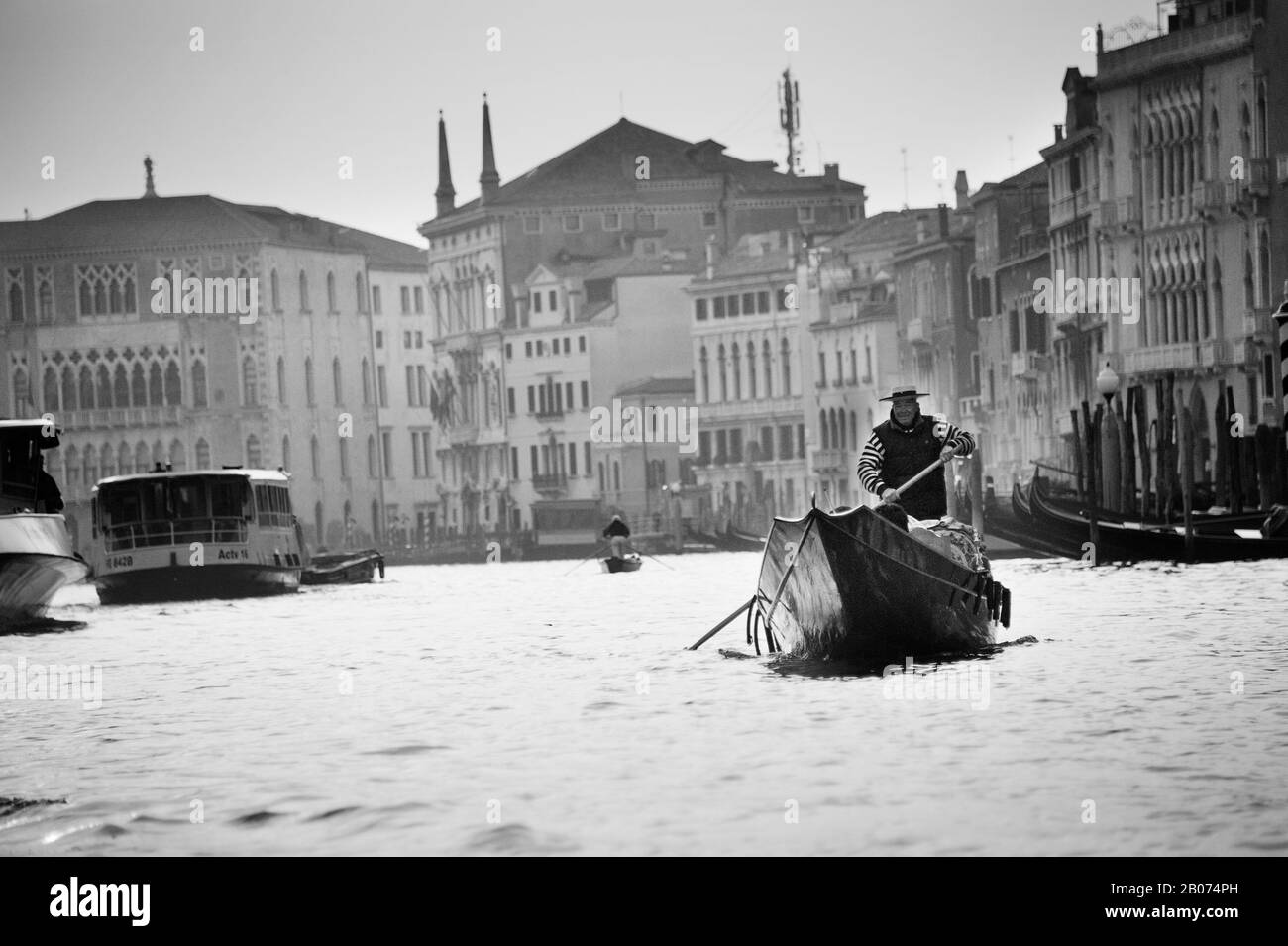 Stadt Venedig, Italien, Europa. Schwarz-Weiß-Bild von Gondolier am Canal Grande mit Wasserbus und Gebäuden im Hintergrund Stockfoto