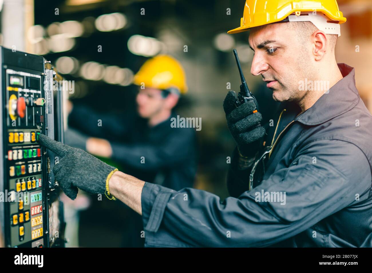 Professioneller Arbeiter-Techniker überwacht an der Maschinensteuertafel und Radio Kommunikation mit dem Kollegen während des Druckens der Taste. Stockfoto
