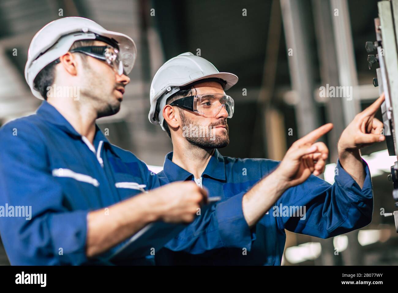 Teamarbeit im Team prüfen, Bedienfeld überprüfen und neuen Mitarbeitern die Bedienung der Maschine im Werk vermitteln. Stockfoto