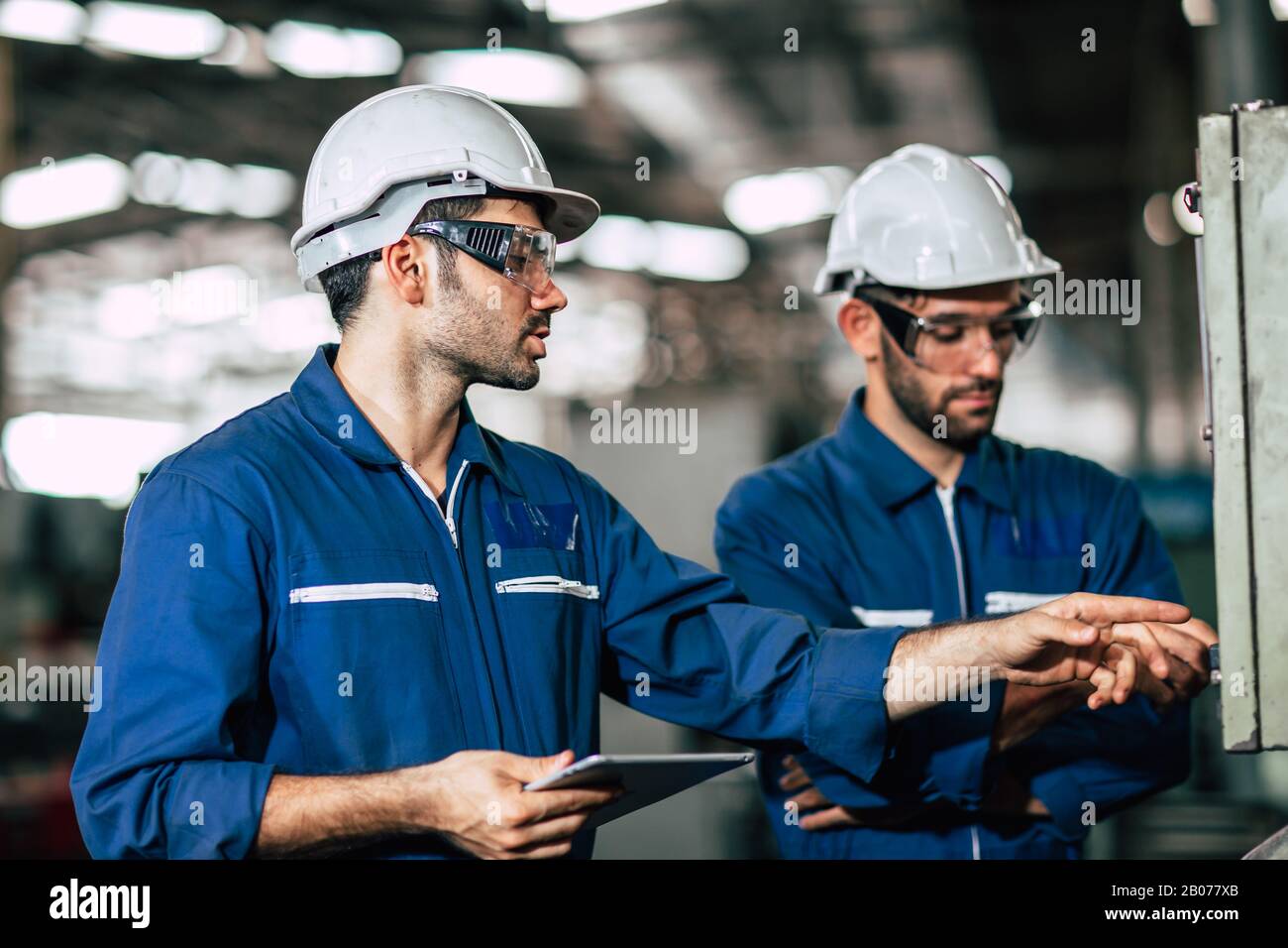 Teamarbeit im Team prüfen, Bedienfeld überprüfen und neuen Mitarbeitern die Bedienung der Maschine im Werk vermitteln. Stockfoto