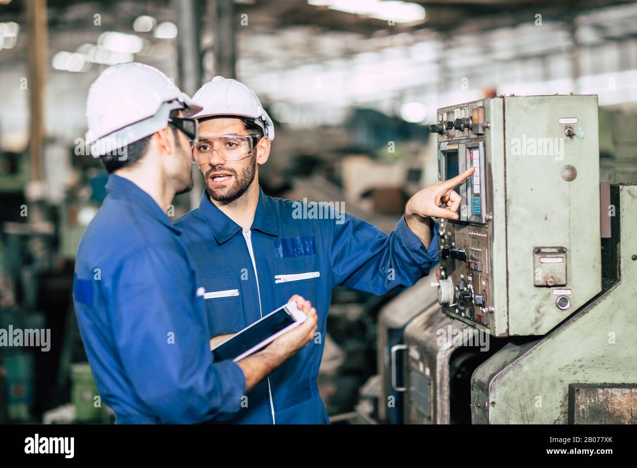 Teamarbeit im Team prüfen, Bedienfeld überprüfen und neuen Mitarbeitern die Bedienung der Maschine im Werk vermitteln. Stockfoto