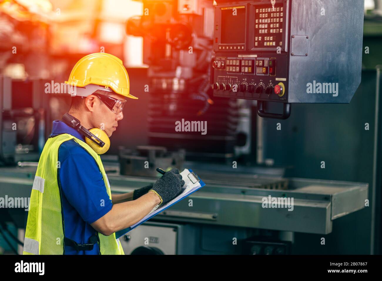 Asiatischer Ingenieur überprüft die Maschine im Werk, Arbeiter schreibt Notiz mit Listenpapier. Stockfoto