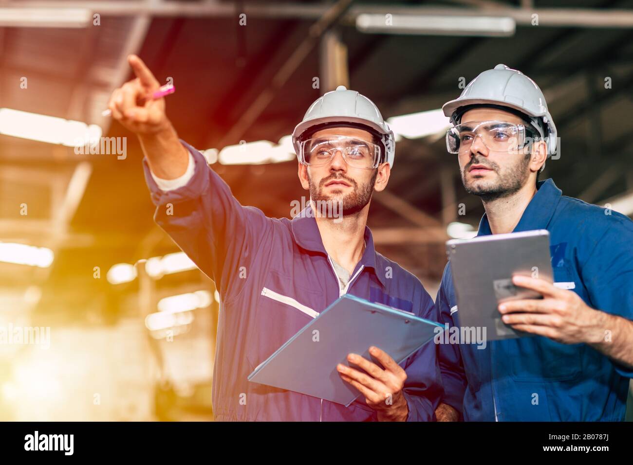 Zwei Techniker arbeiten zusammen mit Sicherheitsuniform und weißem Helm, um in der Industrie zu arbeiten, die Werkstafel zu handhaben. Stockfoto