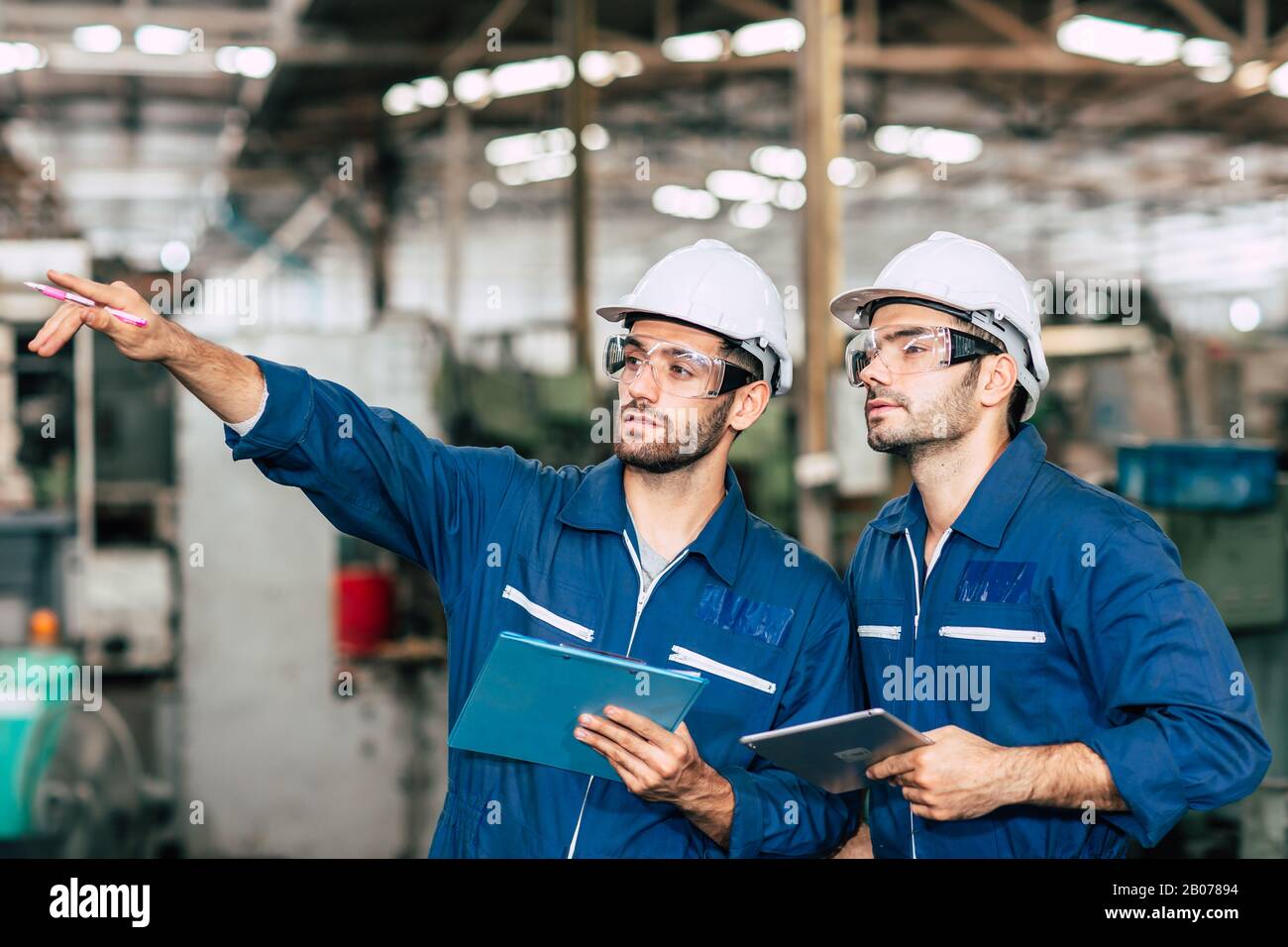 Zwei Techniker arbeiten zusammen mit einem Sicherheitsuniform und einem weißen Helm, um in der Industrie zu arbeiten und die Produktionslinie zu überprüfen. Stockfoto