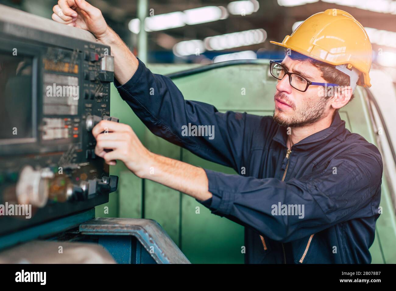 Professionelle Brille für junge Arbeiter, Ingenieur bei CNC-Maschinensteuertafel tragen Sicherheitsanzug und Helm, die in der Industriefabrik arbeiten. Stockfoto