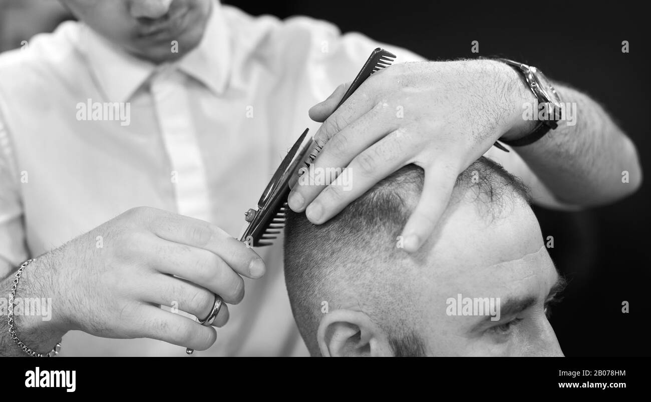 Ein kurzer Haarschnitt für seinen Kunden im modernen Barbershop. Konzept des traditionellen Haarschneidens mit Schere. Schwarz-Weiß-Bild Stockfoto