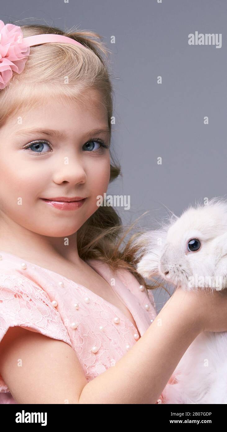 Kleines hübsches Mädchen, das ein Kaninchenbaby hält. Weisses niedliches Haustier im Studio. Frohe ostern Umarmung. Weibliche Person Hand. Lächeln Sie Menschen Kind. Junge Leute. Stockfoto