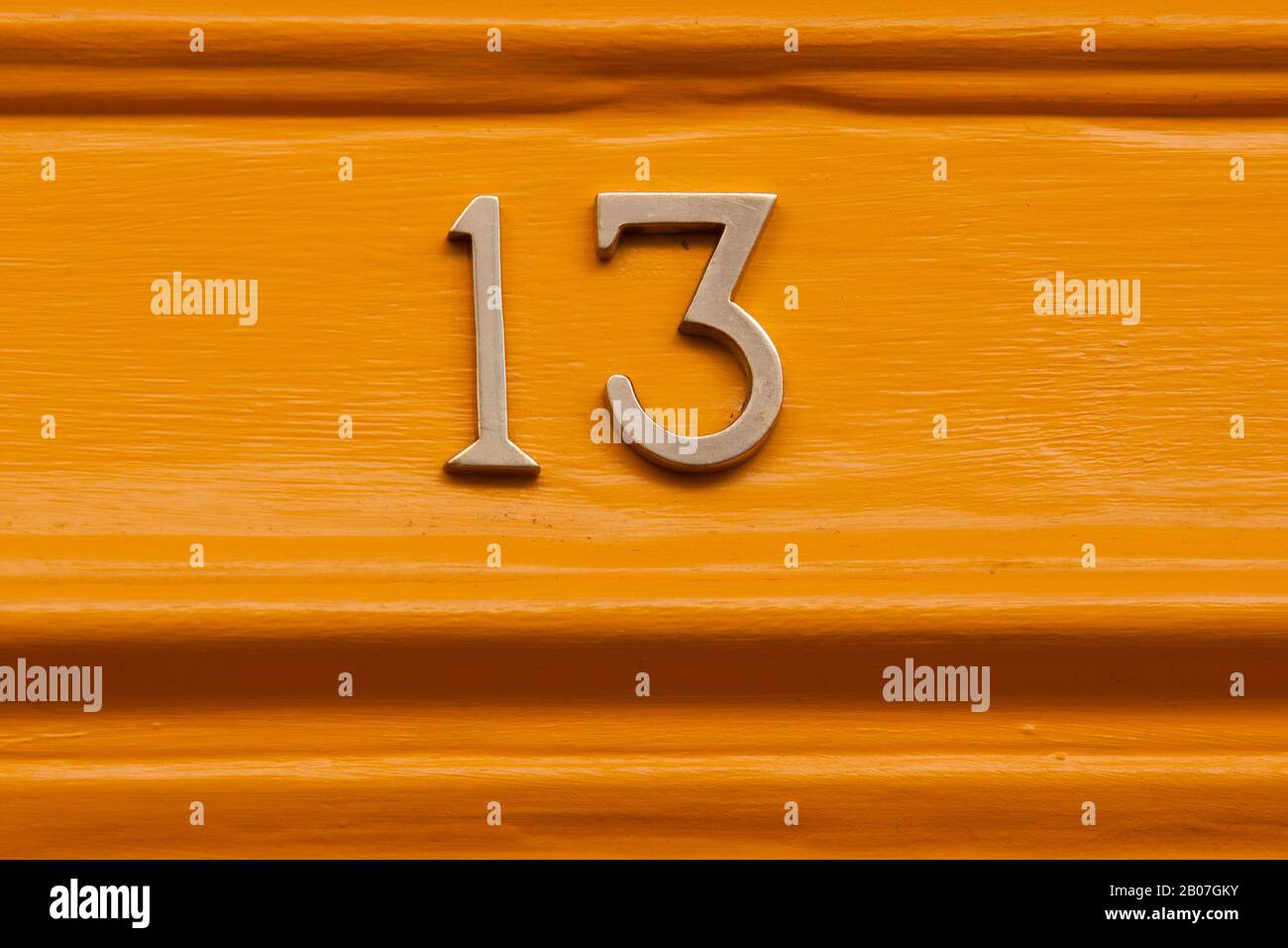 Die Tür aus Messing mit der Nummer dreizehn auf einer orangefarbenen, glänzend bemalten Eingangstür auf einem Anwesen in der Stadt Bath, Somerset, Großbritannien Stockfoto