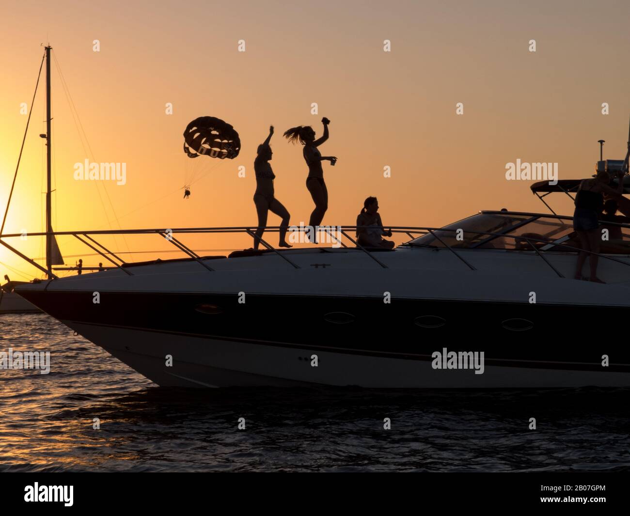 Partygäste auf Ibiza tanzen bei Sonnenuntergang auf einem Boot, das vor der Küste vom Cafe Mambo in der Partyhauptstadt San Antonio auf der Partyinsel Ibiza vor Anker liegt Stockfoto