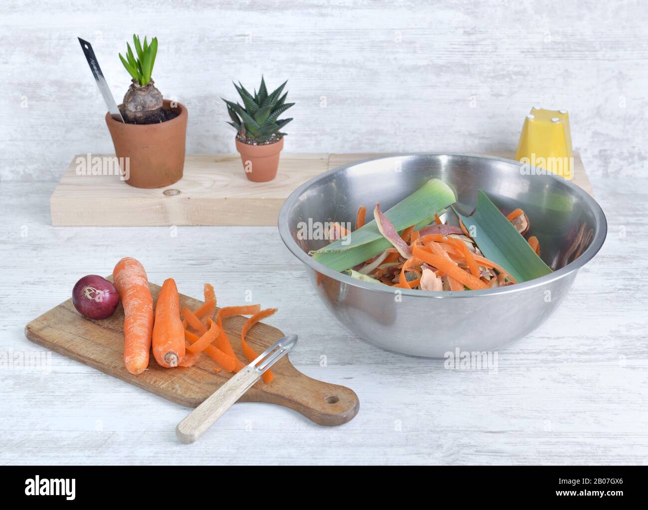 Karotten auf einer Kochplanke und eine Schüssel voller Abfall auf einem Tisch in einer Küche abschälen Stockfoto